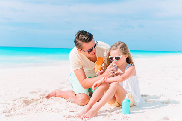 Młody tata nakłada krem na nos córki na plaży. Ochrona przeciwsłoneczna - Zdjęcie, obraz