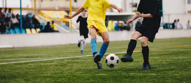 Παίζουν ποδόσφαιρο σε μονομαχία. Νεαροί αθλητές κλωτσάνε ασπρόμαυρες μπάλες ποδοσφαίρου. Νεανική ομάδα ποδοσφαίρου της νεολαίας ανταγωνίζονται στο γήπεδο χόρτο. Τουρνουά θερινού σχολείου ποδοσφαίρου - Φωτογραφία, εικόνα