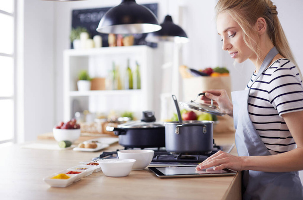 Young woman using a tablet computer to cook in her kitchen - Valokuva, kuva