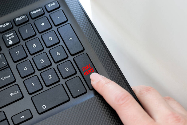 Klávesový roh černého laptopu s ženským prstem kliknutím na falešné tlačítko zprávy. Koncept šíření falešných zpráv, zpráv na internetu - Fotografie, Obrázek