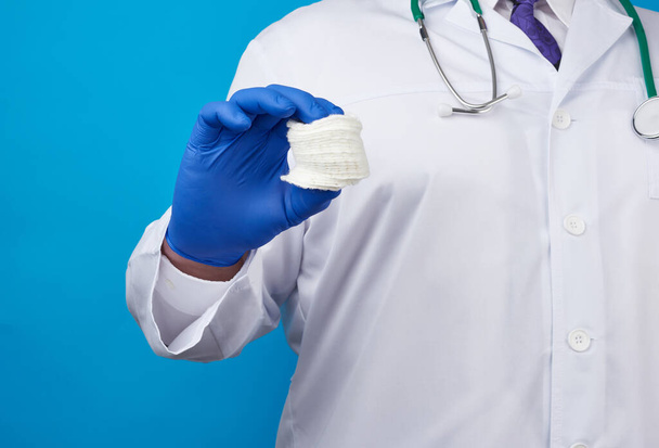 médico masculino em um casaco branco, luvas médicas de látex azul segurando uma pilha de discos cosméticos de algodão, fundo azul
 - Foto, Imagem