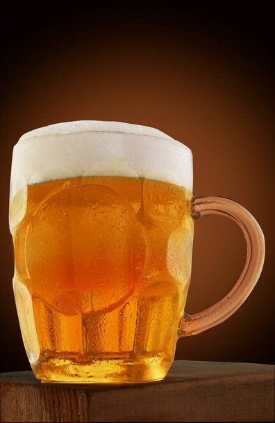 Beer in a mug with foam, on a wooden stand and a brown background. - Foto, Imagem