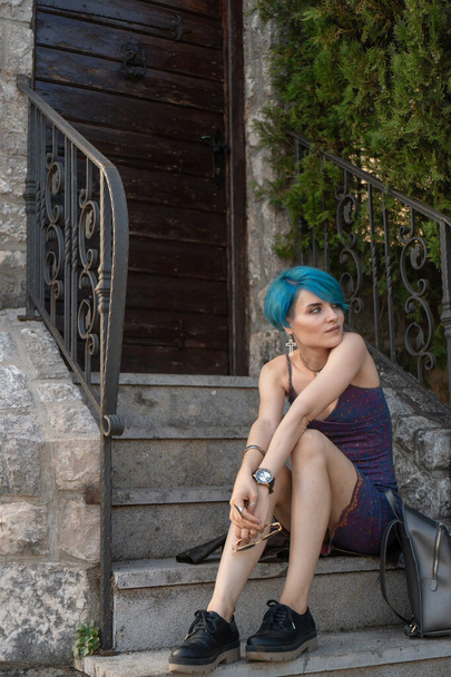 La chica en el vestido se sienta en las escaleras cerca de las puertas de madera cerradas oscuras
 - Foto, Imagen