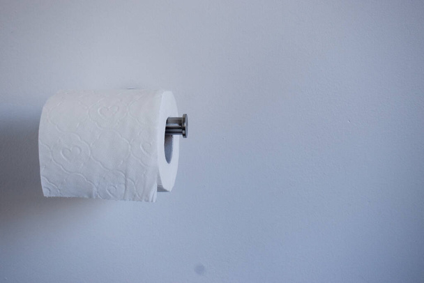 Toaletní papír na držáku u bílé stěny. Toaletní papír panika nákup, hromadění koncept - Fotografie, Obrázek