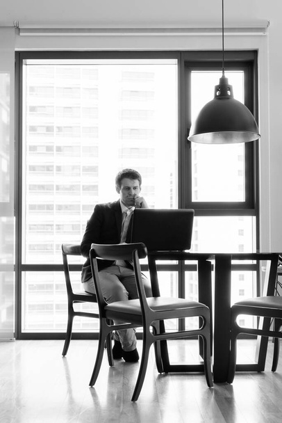 Ritratto di giovane bell'uomo d'affari seduto nella sala da pranzo vicino alla cucina in bianco e nero - Foto, immagini