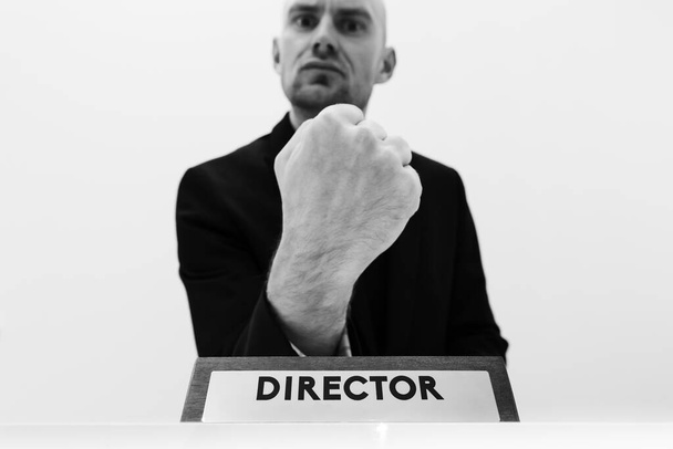 Schwarz-Weiß-Bild eines wütenden männlichen Chefs, der eine Faust mit einem Firmenschild mit Titel zeigt - Direktor vor ihm. - Foto, Bild