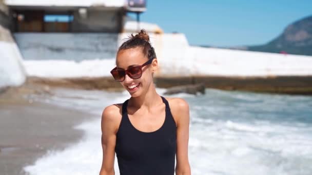 powolny ruch szczupły sexy fitbody uśmiechnięty młoda kobieta w czarny strój kąpielowy spacery wzdłuż plaży morskiej z falami. - Materiał filmowy, wideo