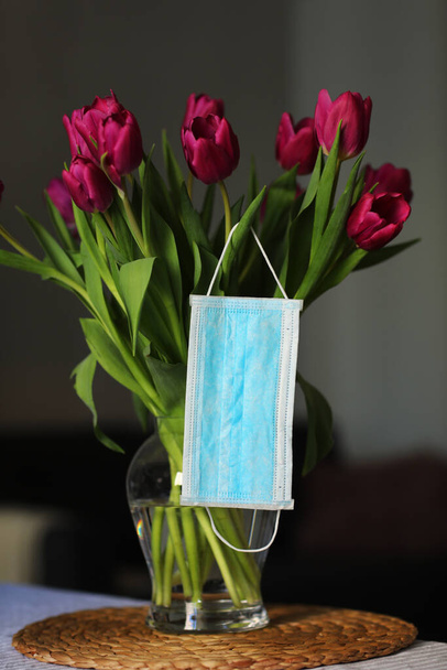 Coronavirus covid 19 karantén koncepció. Húsvéti tavaszi tulipán virág csokor arcorvosi maszkkal az asztalon otthon. szelektív fókusz. - Fotó, kép