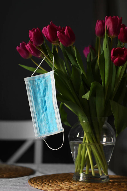 Coronavirus covid 19 karantén koncepció. Húsvéti tavaszi tulipán virág csokor arcorvosi maszkkal az asztalon otthon. szelektív fókusz. - Fotó, kép