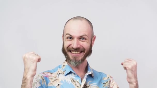 Een gelukkige man met een Hawaïaans shirt die een overwinning viert op een witte achtergrond, slow motion. Emoties van succes, triomf, overwinning, winnen en vieren. - Video