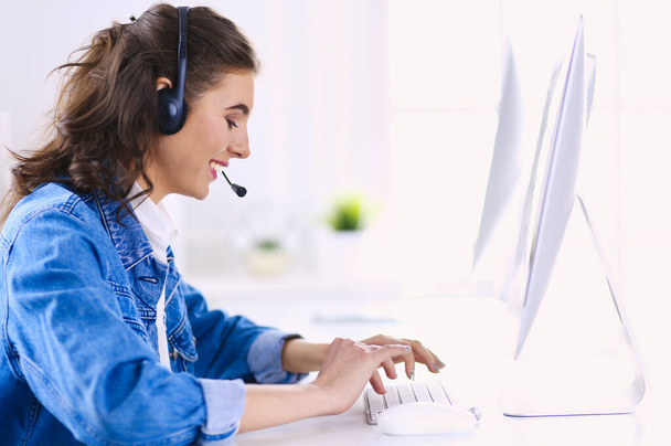 Happy charming young woman sitting and working with laptop using headset in office - 写真・画像
