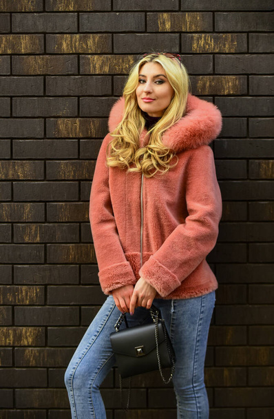 spring summer trend. Fashionable woman in pink fur coat at brick wall. cold season. Autumn or winter look. beautiful stylish woman walking in pink coat. holding purse in hands. street style - Photo, Image