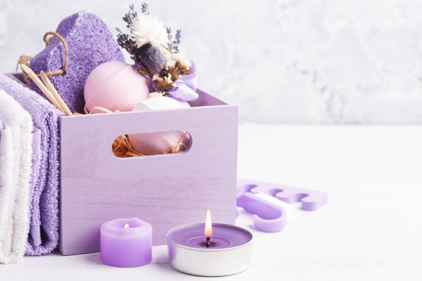 Bombes de bain d'arôme, pierre ponce violette et lavande dans l'arrengement SPA dans une boîte en bois. Serviettes, bougies violettes allumées au premier plan
 - Photo, image