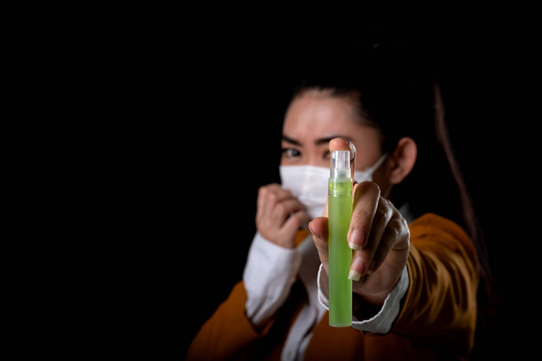 Donna d'affari di giovane donna asiatica che indossa una maschera respiratore N95 con la mano che l'applicazione di spray alcolico dalla bottiglia di plastica o anti batteri per prevenire la diffusione di germi su sfondo nero
 - Foto, immagini