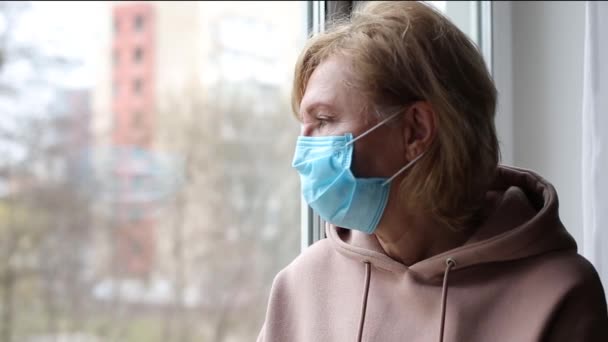 Mujer mayor con máscara médica cerca de la ventana
 - Imágenes, Vídeo