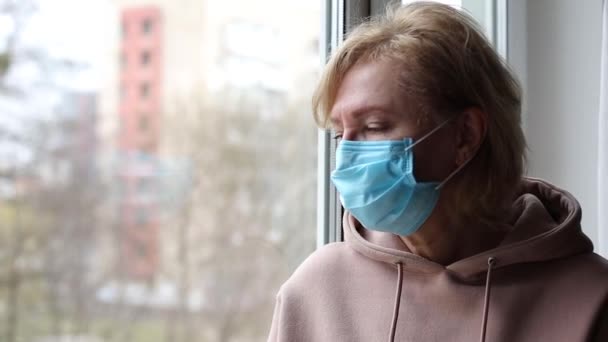 Starsza kobieta w masce medycznej przy oknie - Materiał filmowy, wideo