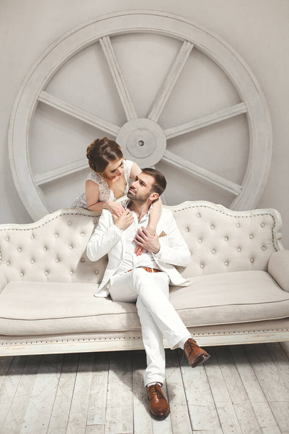 Chic wedding couple groom and bride posing in a white Studio. Happy couple laughing. White dress. White suit. Youth. Wedding. Chandelier. Sofa. The door. - Φωτογραφία, εικόνα