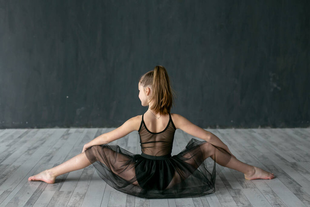 encantadora gimnasta se sienta en el suelo con su espalda a la cámara y realiza divisiones transversales
 - Foto, imagen