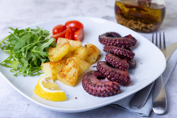 Grilled octopus with fried potatoes, arugula, tomatoes and lemon. Close-up. - Foto, imagen