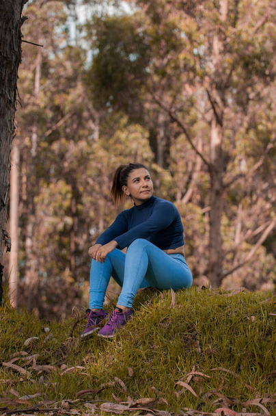obecný portrét mladé ženy sedící na trávě oblečené v modrém uprostřed přírody - Fotografie, Obrázek