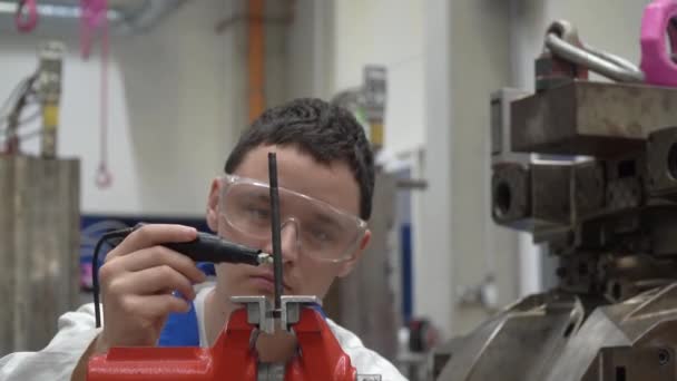 jonge technicus in een fabriek die een machine repareert. man gebruikt een bankschroef om in de fabriek te werken - Video