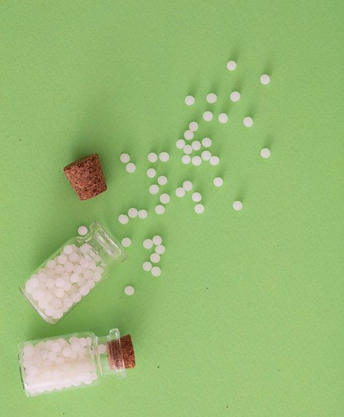 Концепція гомеопатії. Гомеопатичні кульки зі скляної пляшки, зеленого фону. Альтернативні трав'яні таблетки для здоров'я, копіювання простору
 - Фото, зображення
