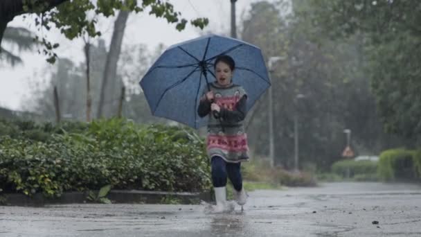 Zpomalený pohyb děvčátka skákajícího v kalužích a držícího deštník v dešti - Záběry, video