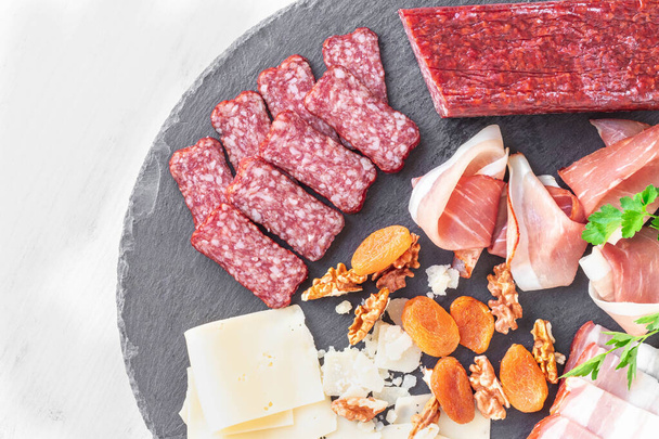 Cheese plate with cheese, prosciutto, nuts. Healthy food, dairy, cheese and meat. Appetizers: Parmesan cheese with ham, salami, sausages on a black plate - Photo, image