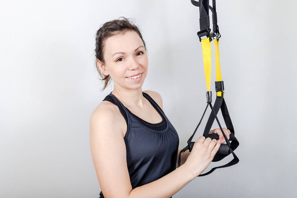 Upper body exercise concept. Image of beautiful woman exercising with suspension straps alone in studio. TRX concept isolated on white background. - Fotografie, Obrázek