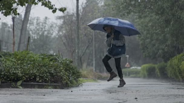 Movimento lento de um menino pulando na chuva torrencial segurando um guarda-chuva
 - Filmagem, Vídeo