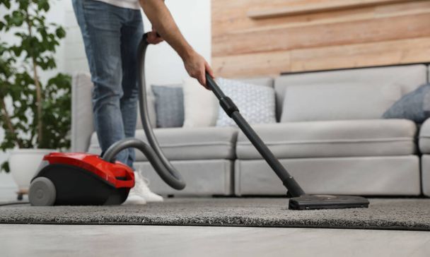 Young man using vacuum cleaner at home, closeup - Fotografie, Obrázek