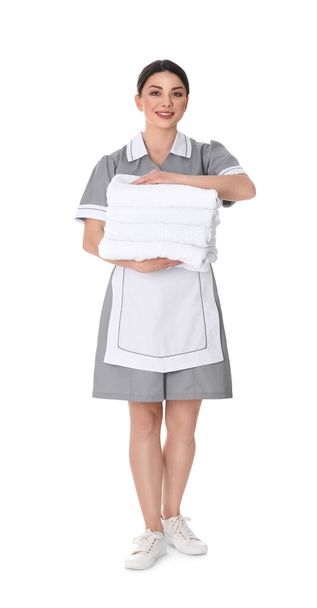 Young chambermaid holding stack of fresh towels on white background - Фото, зображення