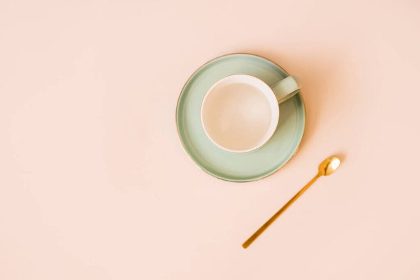Kaunis kahvikuppi, jossa on lautanen ja kultainen lusikka kevyellä taustalla. Näkymä ylhäältä. Litteä
 - Valokuva, kuva