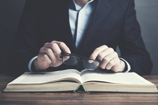 Чоловік читає книгу рукою і окуляри на столі
 - Фото, зображення