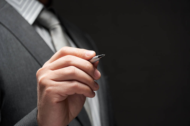 egy toll közelkép üzletember kezét, szürke öltöny, sötét fal háttér - Fotó, kép