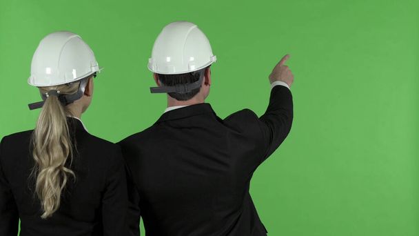 Vista trasera del ingeniero masculino que apunta hacia arriba con el ingeniero femenino, llave del croma
 - Foto, imagen