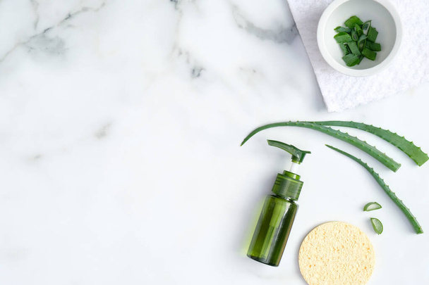 Natural organic cosmetic lotion bottle, sponge and sliced stems aloe vera on marble background. Flat lay, top view. Skin care, SPA, beauty treatment concept. - Fotó, kép