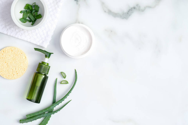 Natural organic SPA cosmetic lotion bottle, sponge and sliced stems aloe vera on marble background. Flat lay, top view. Skin care and beauty treatment concept. - Fotoğraf, Görsel
