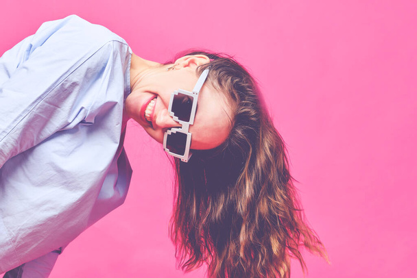 Stilvolles kaukasisches Mädchen in hellblauem T-Shirt und 8-Bit-Brille auf rosa Hintergrund. Kopf zur Seite gesenkt und nach unten. Aus nächster Nähe. Getönt. - Foto, Bild