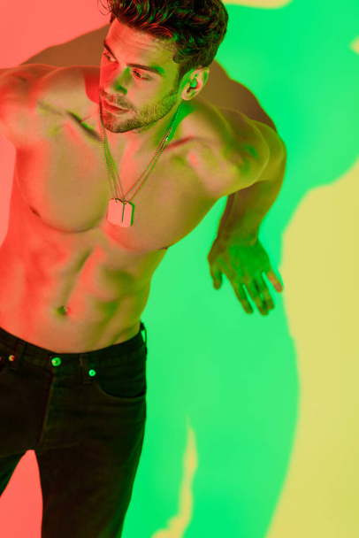 sexy, homme torse nu appuyé sur le mur et regardant loin sur jaune avec des ombres rouges et vertes
 - Photo, image