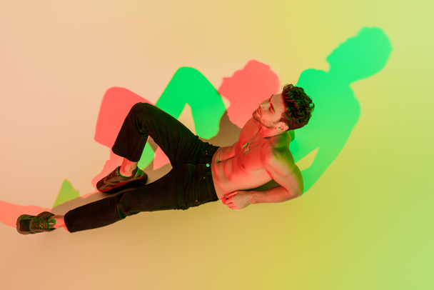 high angle view of sexy, dreamy man in black jeans lying with closes eyes on yellow with red and green shadow - Fotoğraf, Görsel