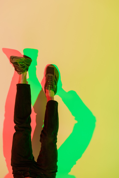 cropped view of male legs in black jeans and sneakers on yellow with red and green shadows, top view - Fotografie, Obrázek