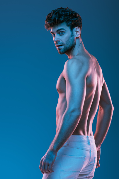 shirtless, muscular man in white jeans looking at camera isolated on blue - Foto, imagen