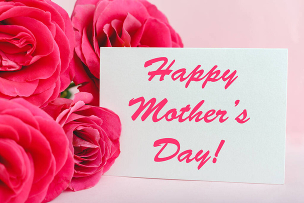 Happy Mothers Day text on gift card in flower bouquet of pink roses on pink background. Greeting card for Mom. Flower delivery, Congratulations card in flowers for women. Greeting card in roses. - Fotó, kép