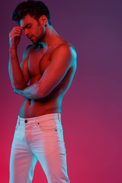 sexy, confident man looking at camera while posing on purple background with gradient - Foto, afbeelding