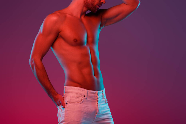 cropped view of sexy, shirtless man holding hand in back pocket while posing on purple background with gradient - Foto, imagen