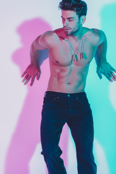 sexy shirtless man in dark blue jeans leaning on wall on background with blue and violet shadows - Foto, Imagen