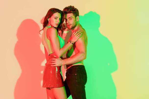 feliz joven pareja abrazando mientras mira a la cámara en el fondo amarillo con sombras rojas y verdes
 - Foto, imagen