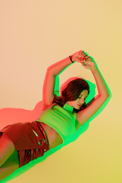 top view of seductive, trendy girl lying with closed eyes on yellow background with green and red shadows - Valokuva, kuva