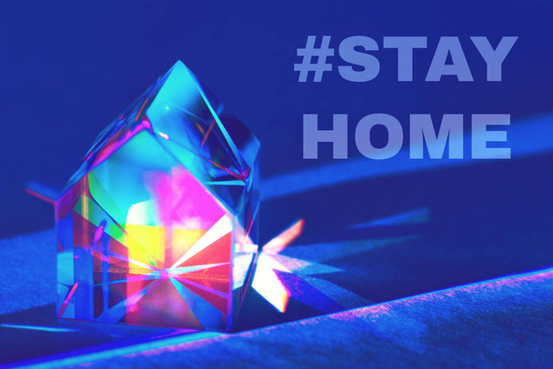 Primer plano de la casa de prisma de vidrio de colores sobre fondo azul de moda con refracción de la luz del arco iris y sombras con texto STAY HOME. Concepto de prevención de la propagación del coronavirus
. - Foto, imagen